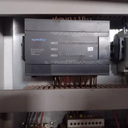 Szary sterownik logiczny programowalny MASTER-K120S, model K7M-DR30UE, zamontowany w szafie sterowniczej z widocznymi przewodami i innymi elementami automatyki.