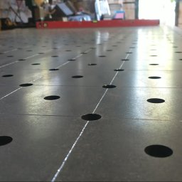 Manufaktura Spawalnictwa Adam Grześkowiak - Stół spawalniczy z otworami i poziomnicą w tle, ukazujący precyzję wykonania i gotowość do pracy. Metalowa konstrukcja z regularnym układem otworów.