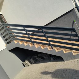 Manufaktura Spawalnictwa Adam Grześkowiak - Zewnętrzne schody z metalową balustradą, prowadzące do budynku o nowoczesnej architekturze. Widoczne detale wykończenia i ułożona kostka brukowa.