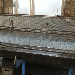 Manufaktura Spawalnictwa Adam Grześkowiak - Konstrukcja z metalowej siatki na stole warsztatowym z narzędziami, w tle ceglana ściana i butla z gazem. Elementy mocowane za pomocą zacisków śrubowych.