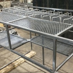 Manufaktura Spawalnictwa Adam Grześkowiak - Konstrukcja metalowa z perforowanymi półkami i uchwytami, surowy stan, widoczne spawy, warsztatowe otoczenie, detale łączeń, perspektywa z boku.