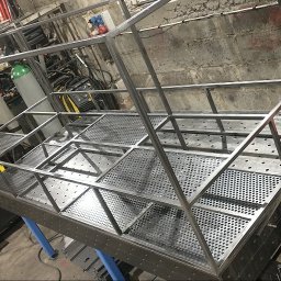 Manufaktura Spawalnictwa Adam Grześkowiak - Metalowa konstrukcja z perforowanymi elementami, spawana na stole warsztatowym. W tle widoczny sprzęt spawalniczy i narzędzia w warsztacie.