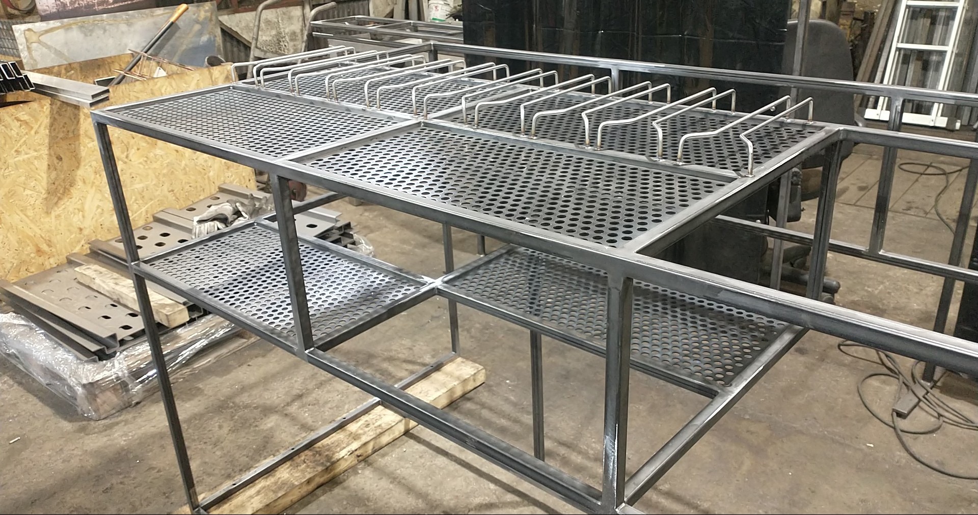 Konstrukcja metalowa z perforowanymi półkami i uchwytami, surowy stan, widoczne spawy, warsztatowe otoczenie, detale łączeń, perspektywa z boku.