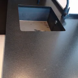 Czarny, teksturowany blat kuchenny z wbudowanym, czarnym zlewozmywakiem i nowoczesną, giętką baterią w kolorze grafitowym.