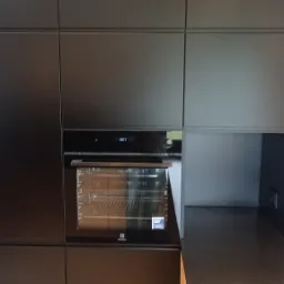 Matowa, czarna zabudowa kuchenna z piekarnikiem Electrolux i blatem z ciemnego kamienia.