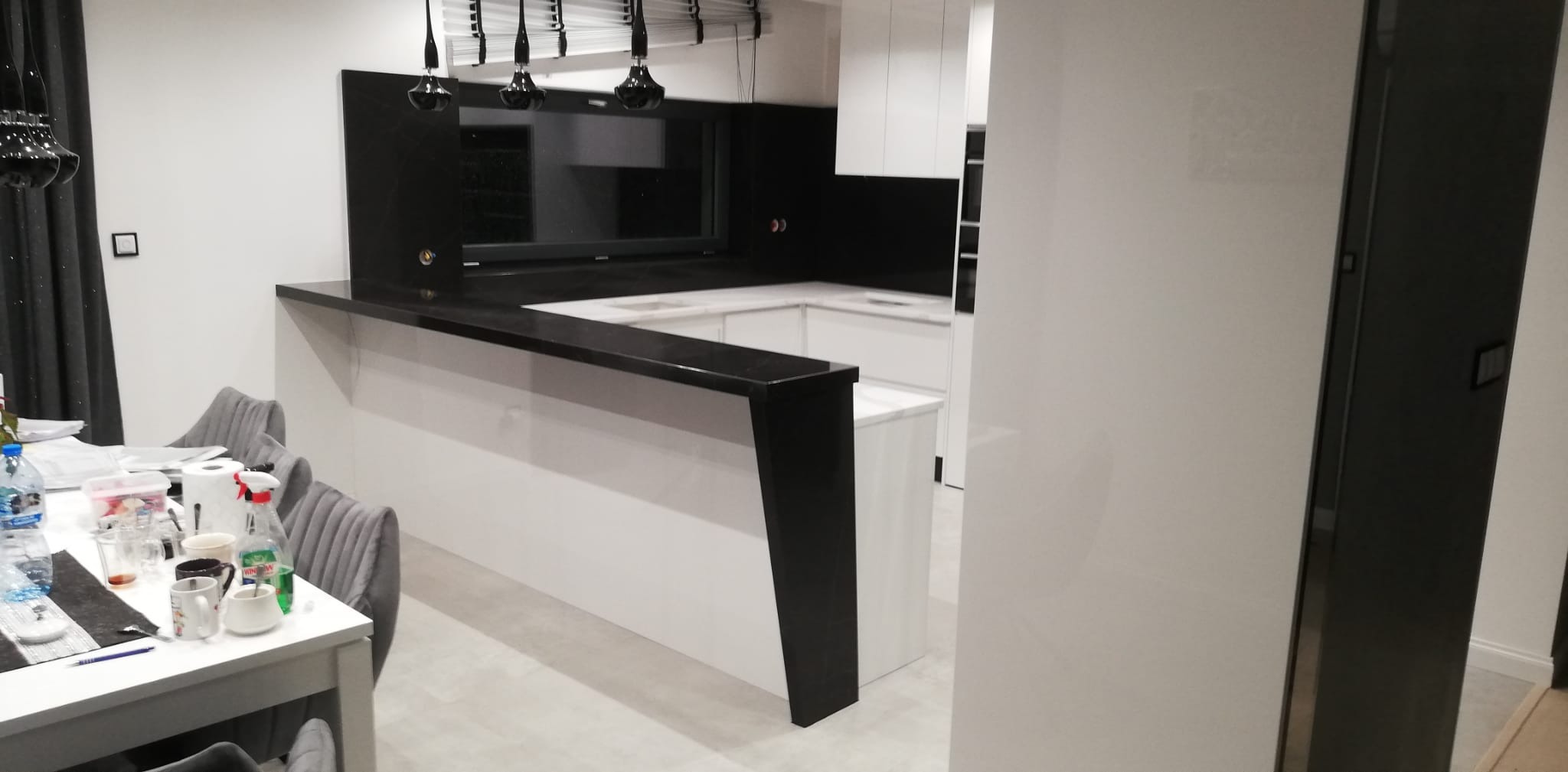 Nowoczesna kuchnia w Ostrołęce z czarnym blatem i elementami wykończeniowymi, widoczny stół z krzesłami i drobne przedmioty codziennego użytku.