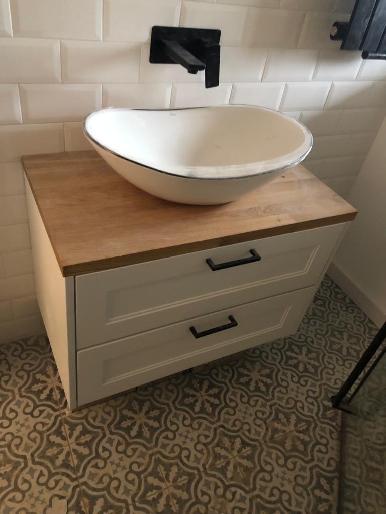 Umywalka nablatowa w kształcie misy, osadzona na szafce z dwoma szufladami i drewnianym blatem, czarna bateria ścienna, wzorzysta podłoga.