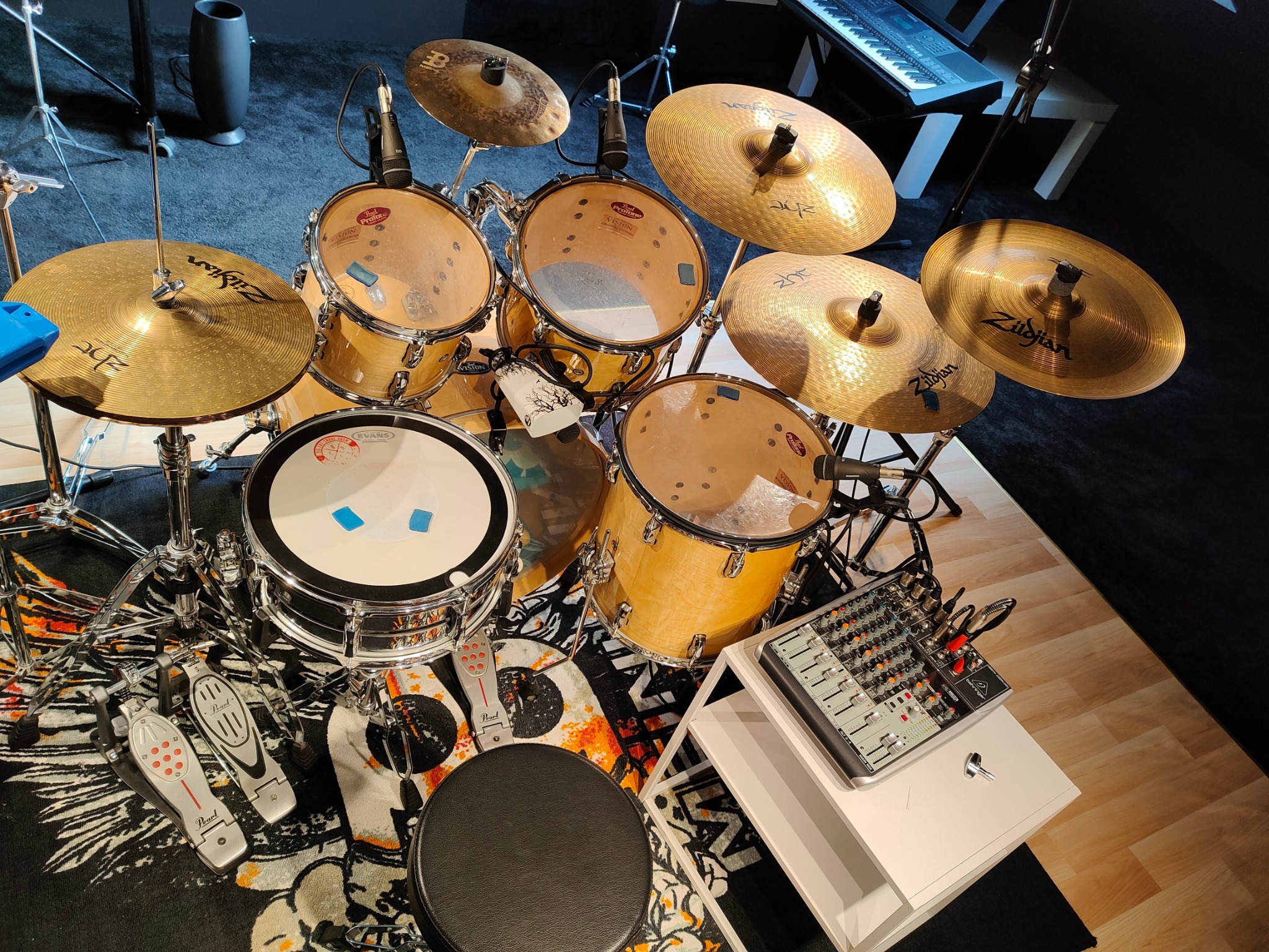 Zestaw perkusyjny Pearl Vision w jasnym wykończeniu, z talerzami Zildjian, mikrofonami, mikserem audio i stołkiem, ustawiony na wzorzystym dywanie w studiu.