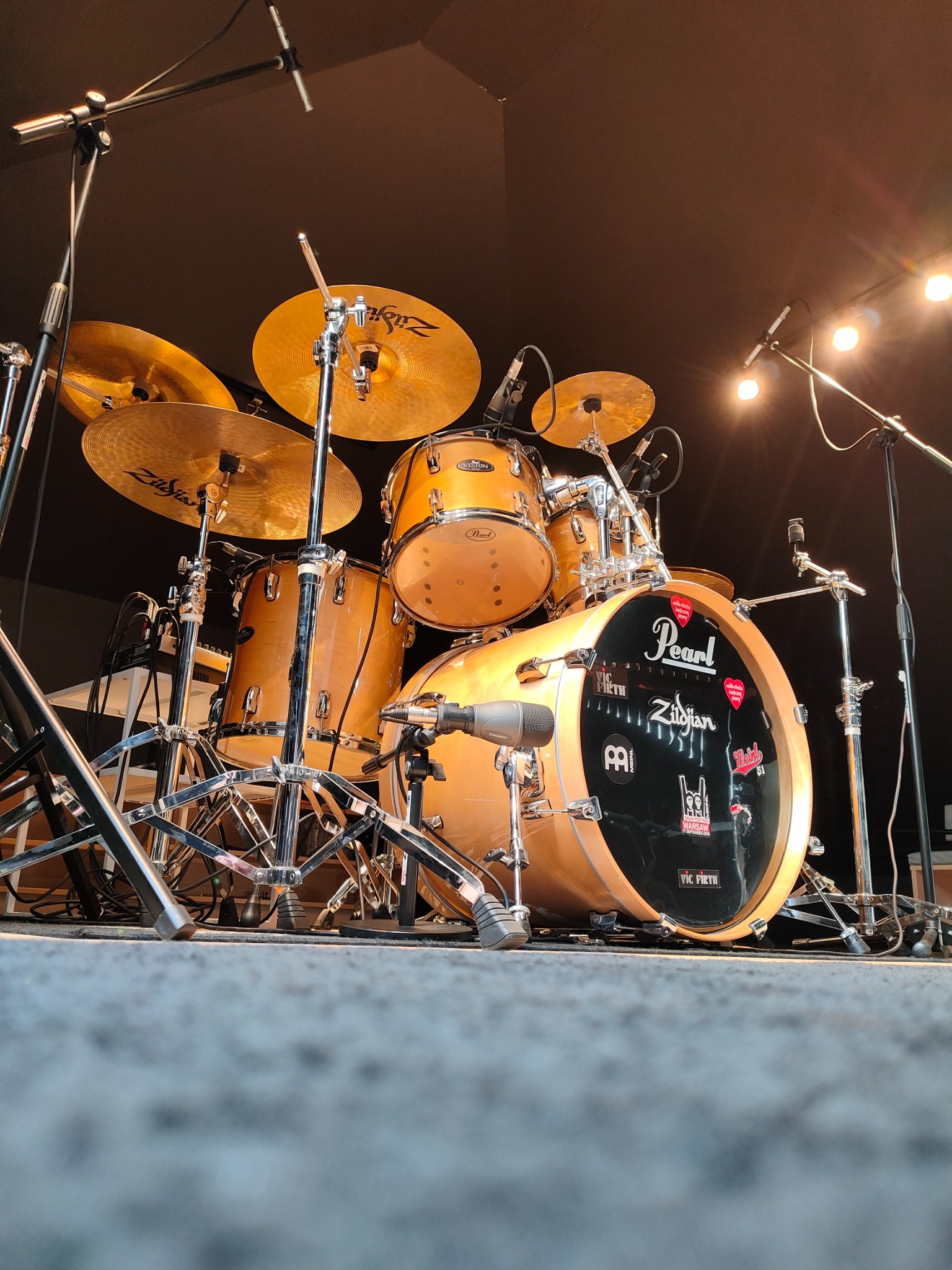 Zestaw perkusyjny Pearl z talerzami Zildjian, mikrofonami i naklejkami, ustawiony na scenie pod światłami, widziany z niskiej perspektywy.