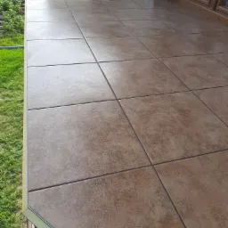 Beżowe płytki ceramiczne ułożone na tarasie, widok z góry, na zewnątrz trawnik i fragment okna.