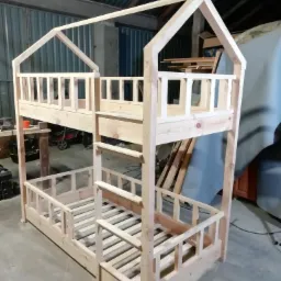 Surowe drewniane łóżko piętrowe w kształcie domku, z barierkami, w warsztacie, przed malowaniem.