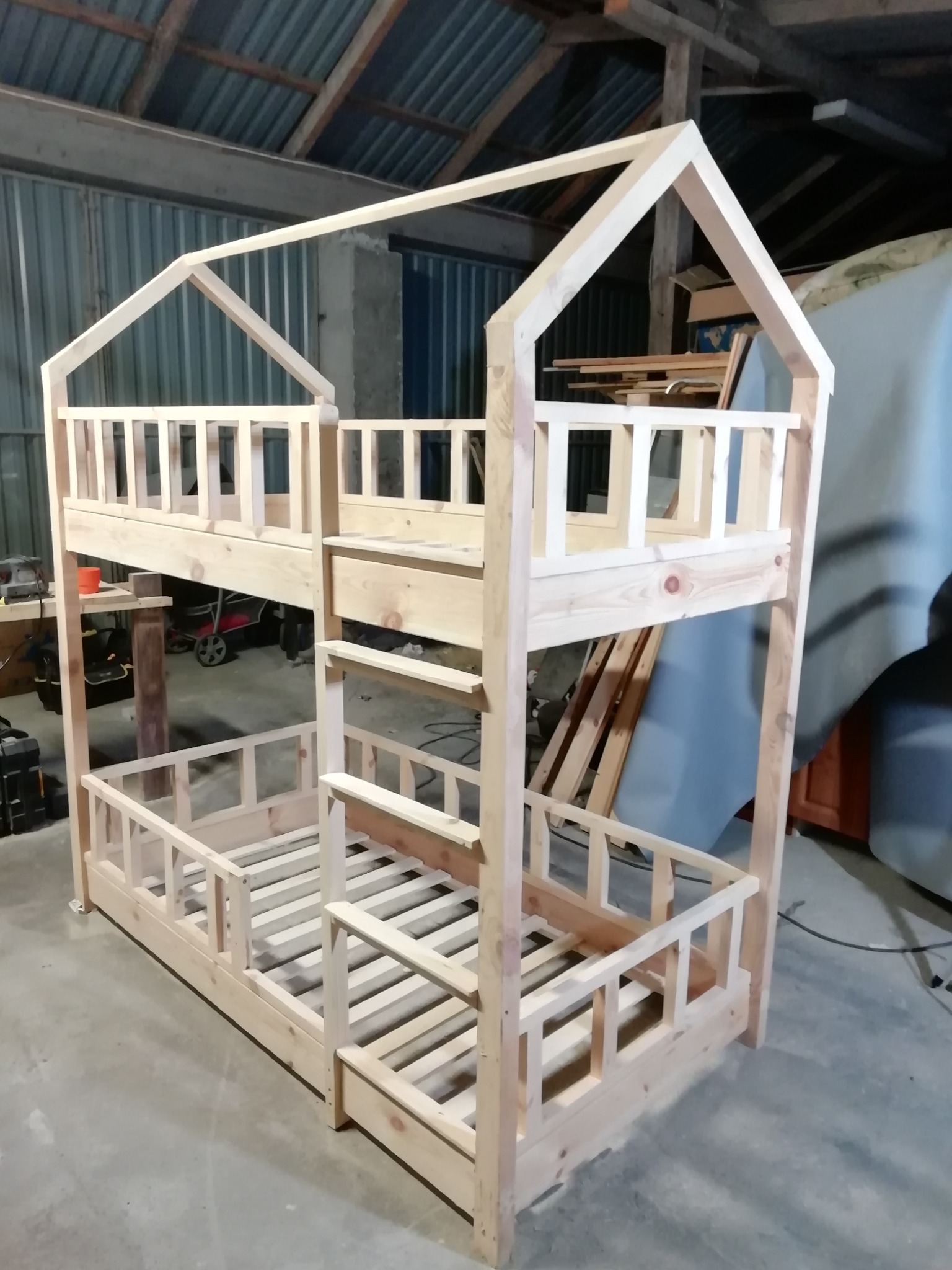 Surowe drewniane łóżko piętrowe w kształcie domku, z barierkami, w warsztacie, przed malowaniem.