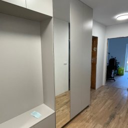 Roman Jaśkiewicz JASK-MEBLE - Jasnoszara szafa wnękowa z lustrem na korytarzu, widoczny fragment podłogi imitującej drewno i dokument leżący na półce.