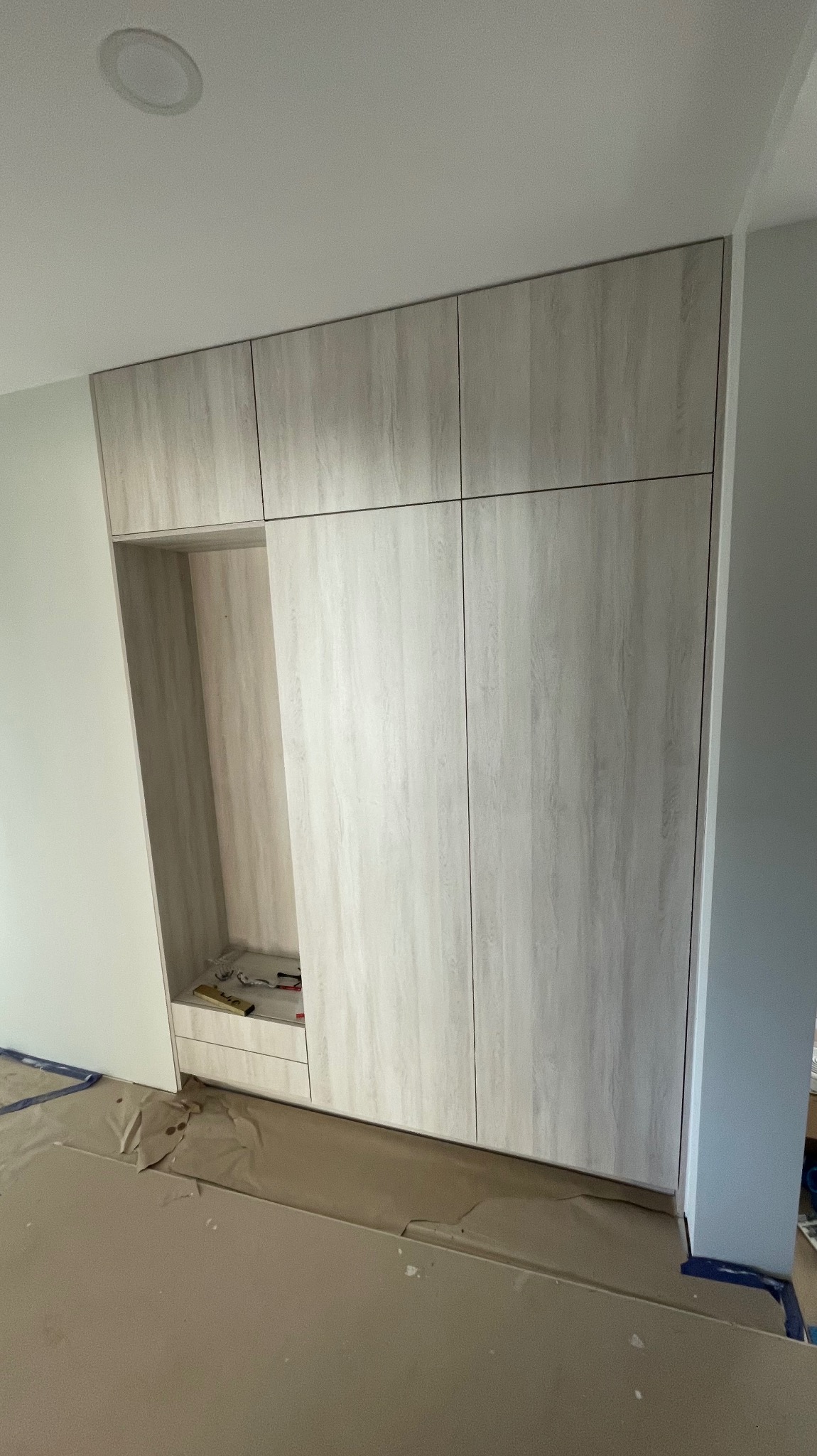 Montaż szafy wnękowej z jasnego drewna, widoczne narzędzia i zabezpieczenia podłogi.