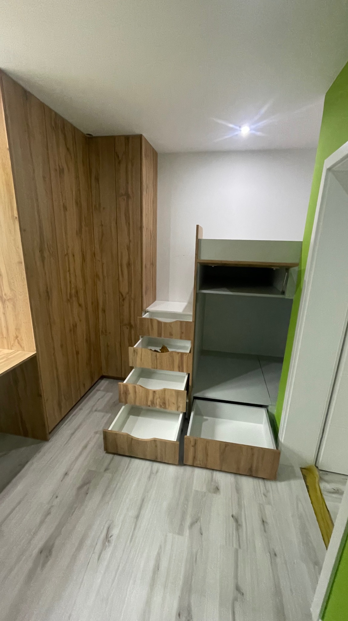 Drewniana szafa wnękowa z otwartymi szufladami w jasnym wnętrzu, widoczne panele podłogowe imitujące drewno.