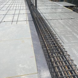 ALEXBUD ALIAKSEI MATSKEVICH - Zbrojenie pionowe w szalunku na stropie budynku w trakcie budowy, widoczne siatki zbrojeniowe na powierzchni szalunku.