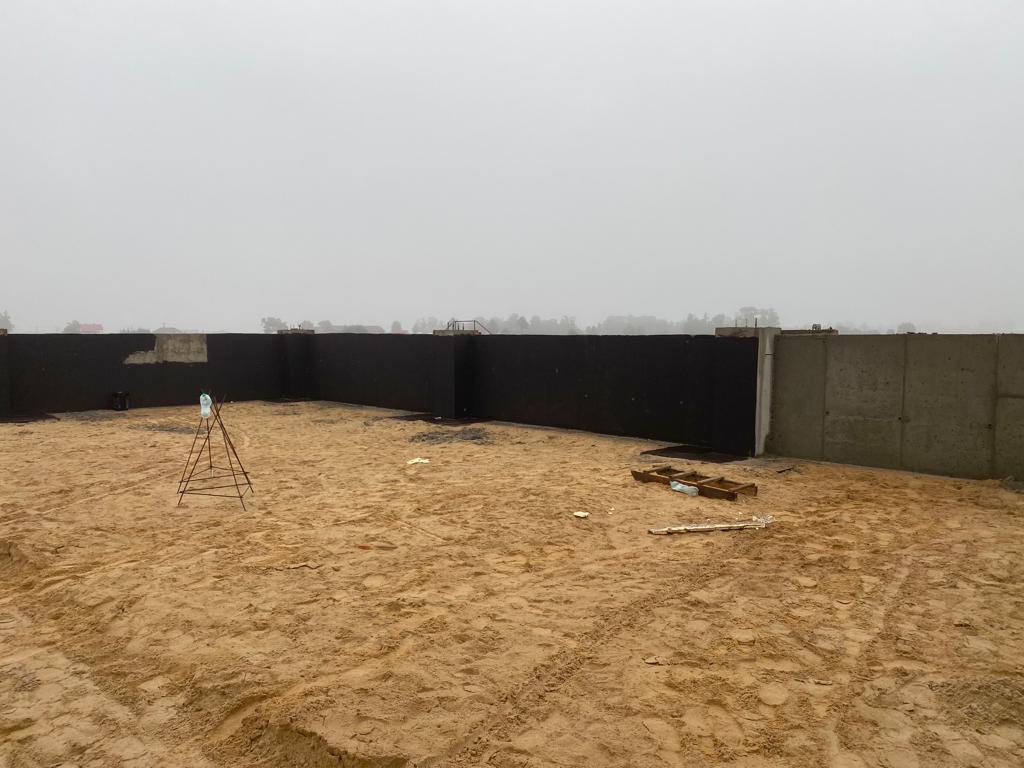 Wykop pod fundamenty z widocznymi ścianami szalunkowymi, zbrojeniem i piaskiem na placu budowy w pochmurny dzień.