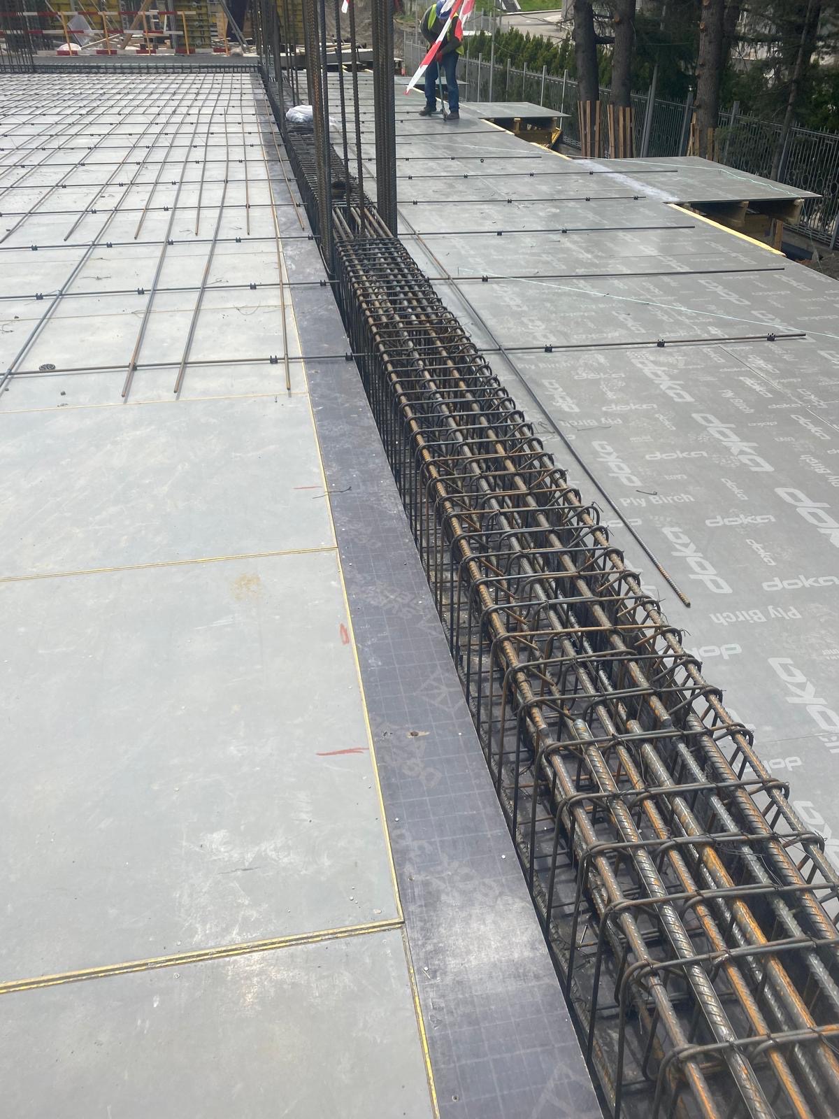 Zbrojenie pionowe w szalunku na stropie budynku w trakcie budowy, widoczne siatki zbrojeniowe na powierzchni szalunku.