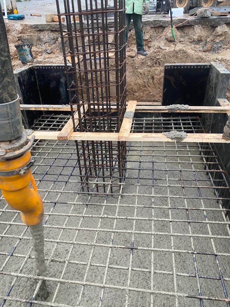 Wylewanie betonu na siatkę zbrojeniową fundamentu z widocznymi szalunkami i wystającą konstrukcją zbrojeniową słupa.