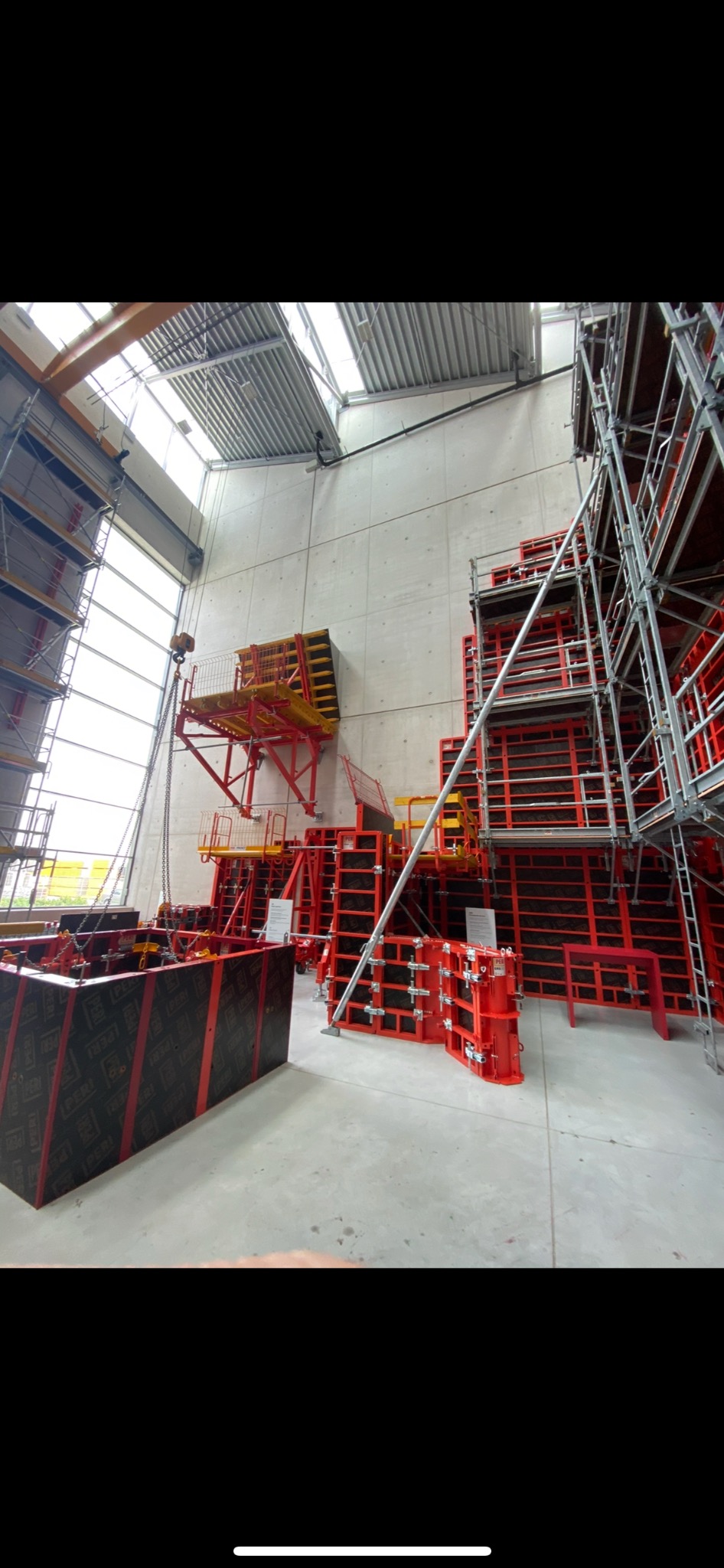 Wnętrze hali z przygotowanymi szalunkami do betonowania, widoczne rusztowania i elementy konstrukcyjne, surowe betonowe ściany.