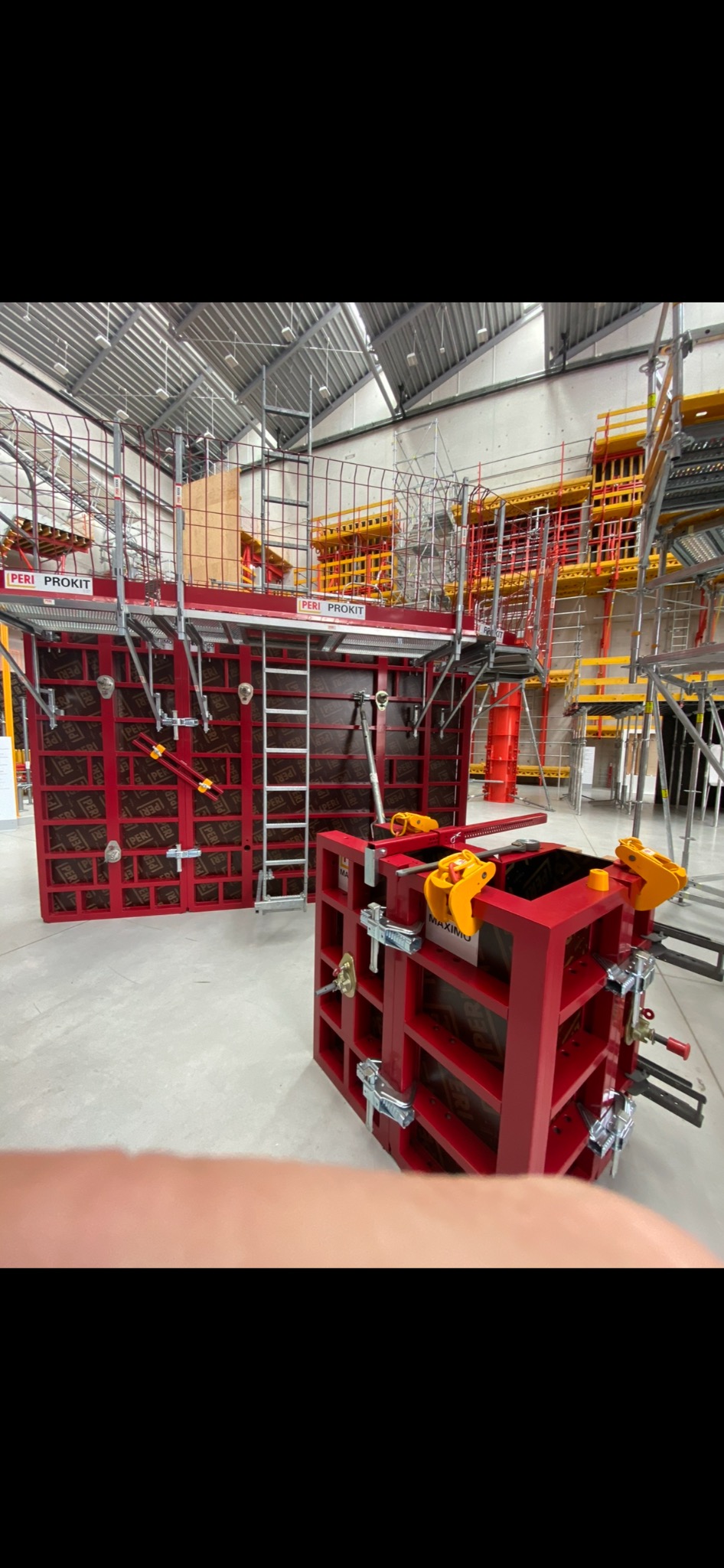 Czerwone, metalowe szalunki PERI PROKIT i MAXIMO, przygotowane do wylania betonu, widoczne na tle hali produkcyjnej z elementami rusztowań.