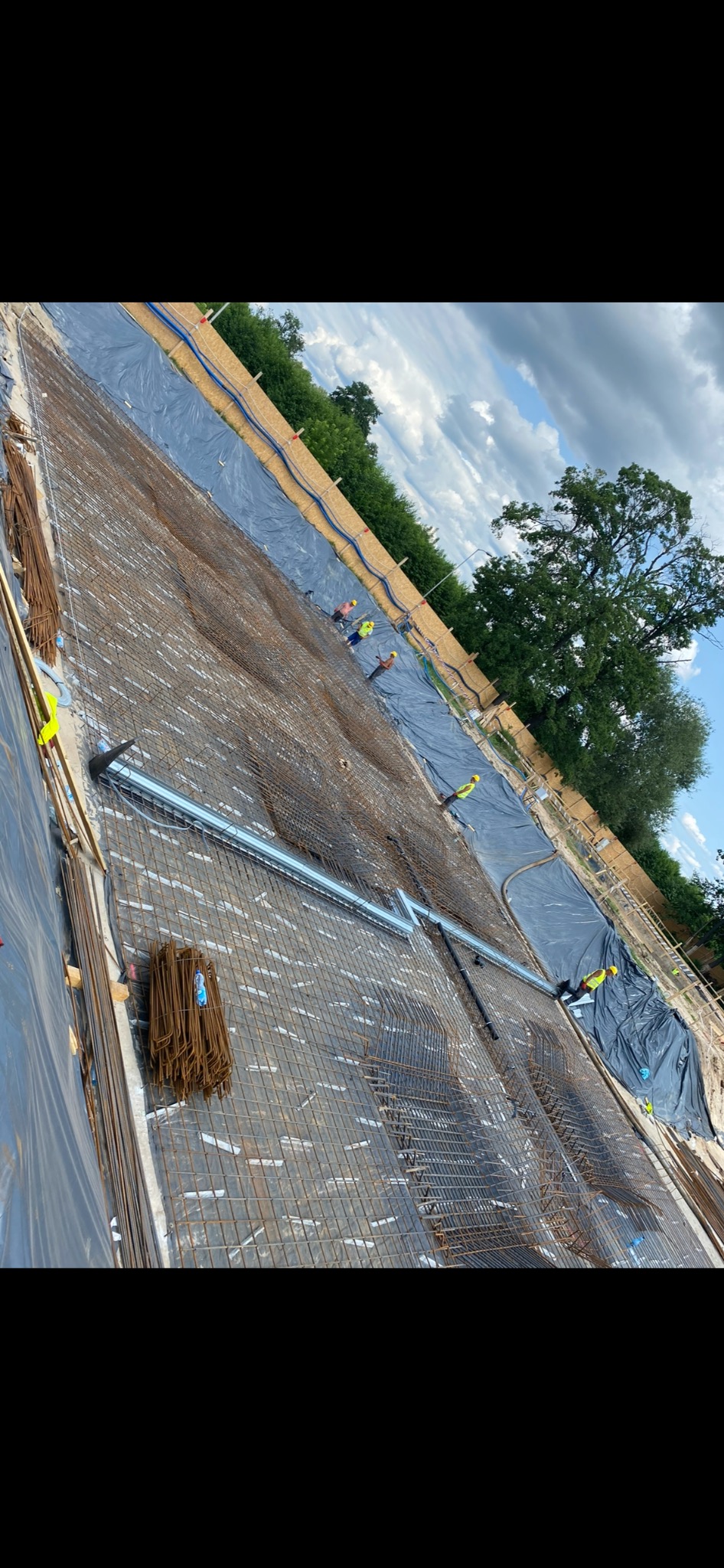 Siatka zbrojeniowa ułożona na folii w wykopie fundamentowym, widoczni pracownicy w kamizelkach odblaskowych, przygotowanie do wylewania betonu.