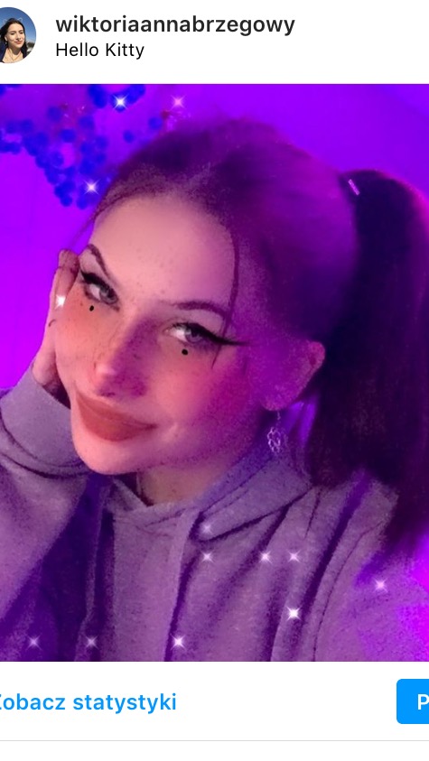 Portret młodej kobiety z wyrazistym makijażem oczu, sztucznymi piegami i błyszczącymi dodatkami, oświetlony fioletowym światłem.