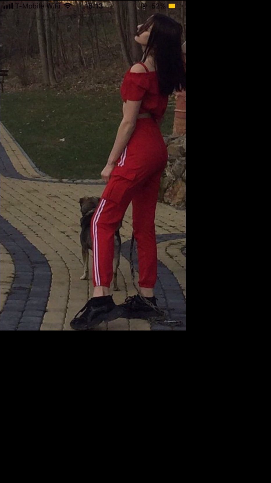 Kobieta w czerwonym dresie z psem na spacerze po brukowanym chodniku w parku.