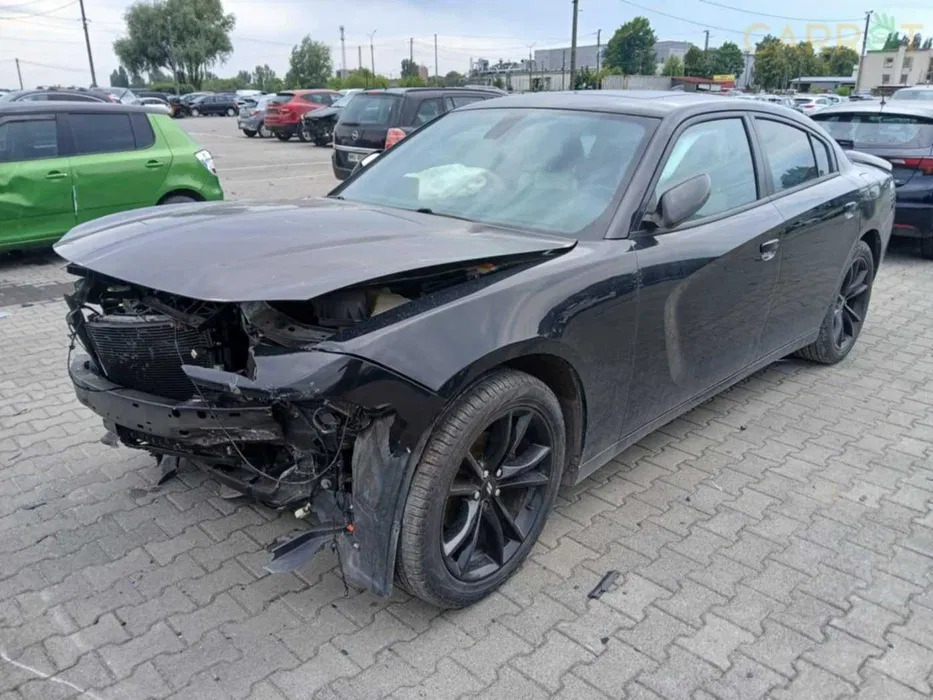 Uszkodzony czarny samochód osobowy na parkingu, widoczne zniszczenia przodu pojazdu, w tle inne auta. Brakujące elementy karoserii.