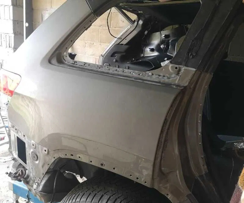 Szary samochód w trakcie naprawy blacharskiej, widoczne uszkodzenia karoserii i przygotowanie do spawania. Detal z bliska, oświetlenie warsztatowe.