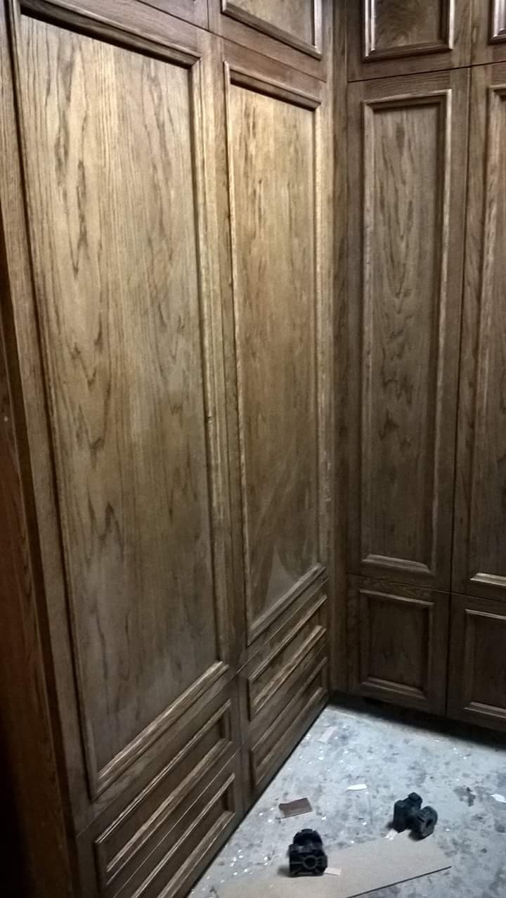 Fragment narożnej zabudowy meblowej z drewna dębowego, widoczne szafki i szuflady z frezowanymi frontami, na podłodze resztki po montażu.