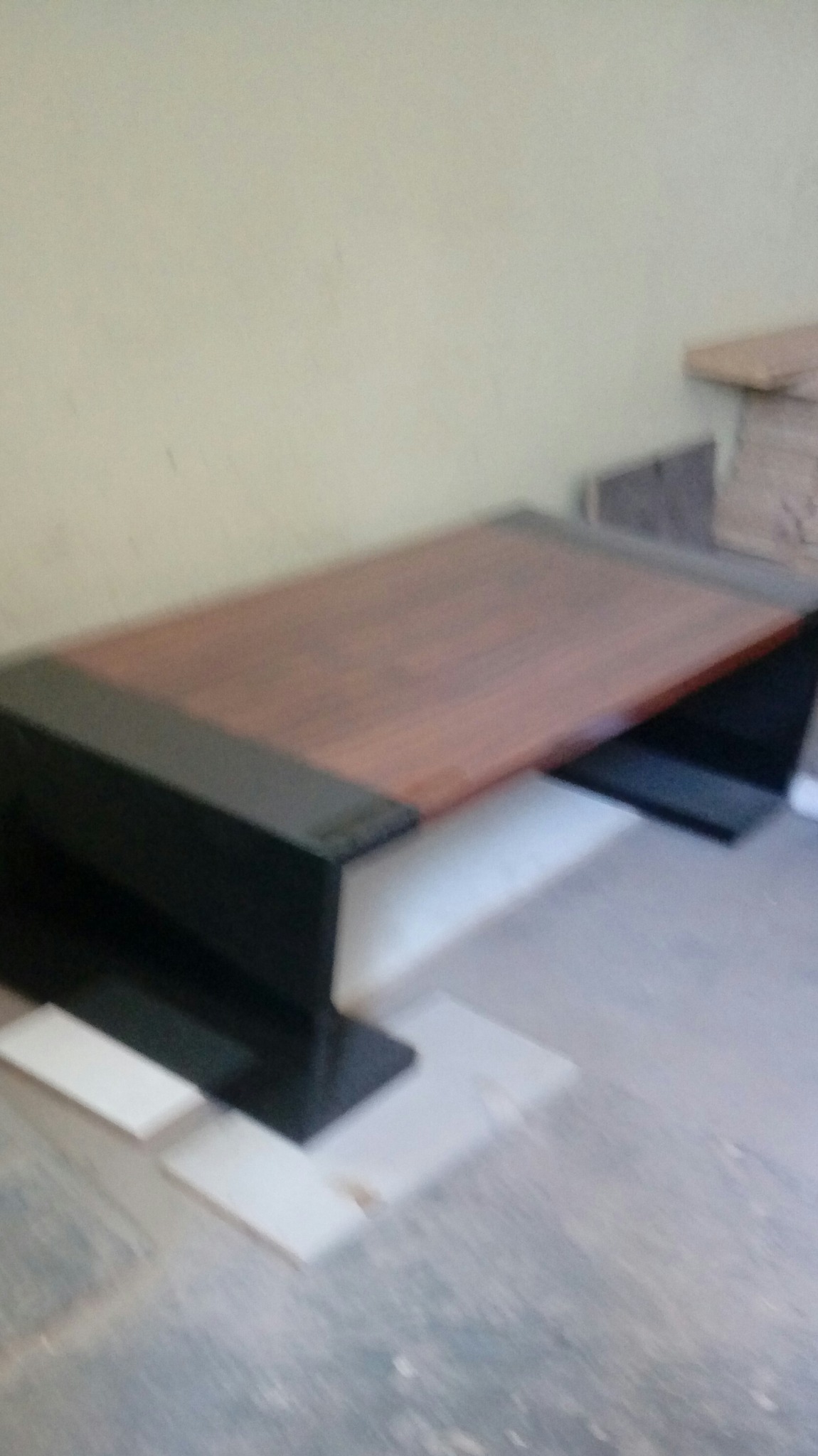 Niedokończony montaż blatu drewnianego z czarnymi krawędziami, widoczne płytki podłogowe w tle, słabe oświetlenie.