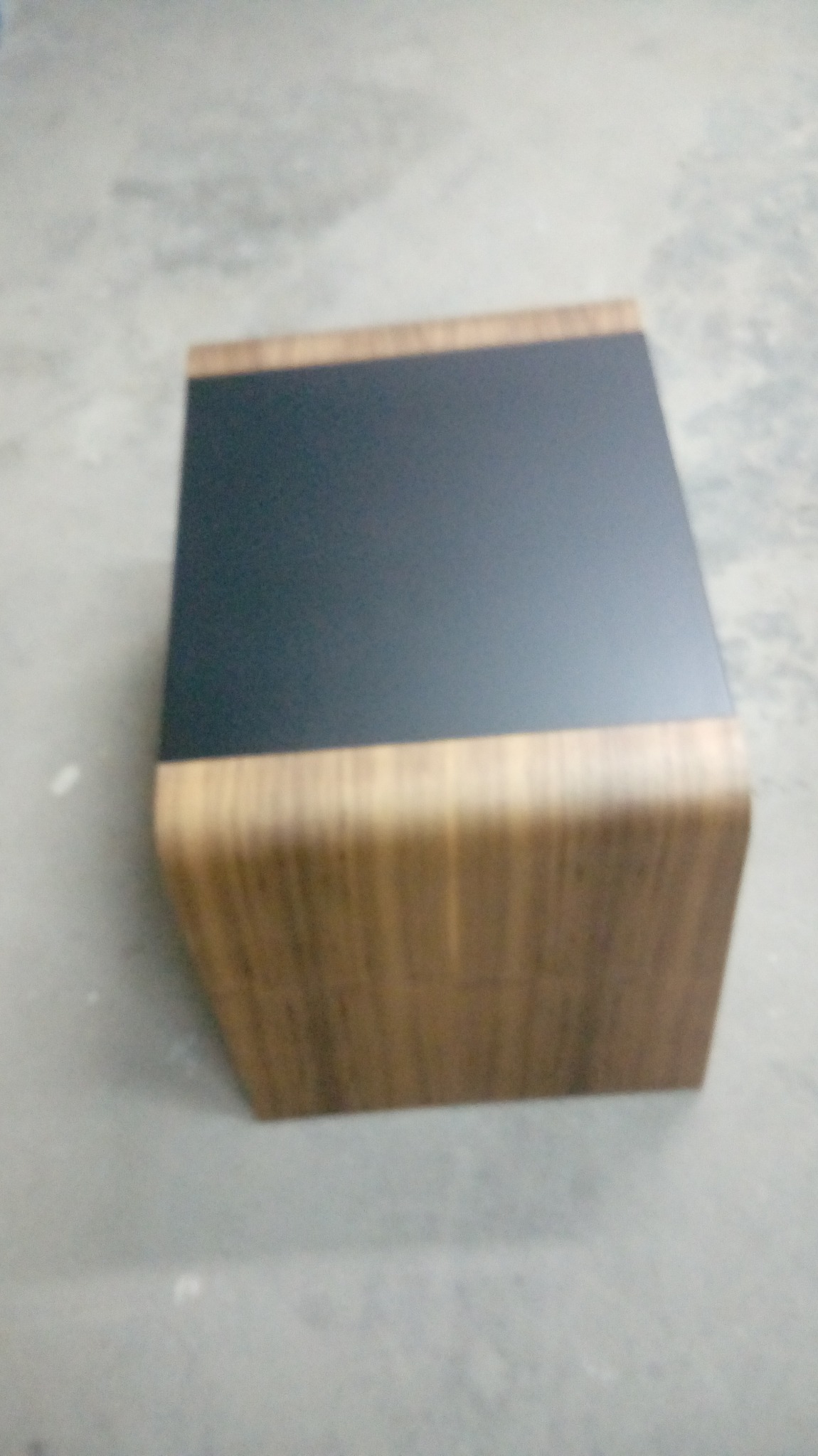 Niski stolik kawowy z blatem w kolorze antracytu i zaokrąglonymi bokami w okleinie drewnopodobnej, ustawiony na szarym tle.