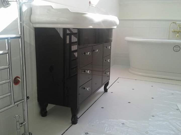 Czarna szafka łazienkowa z umywalką w stylu retro, na tle białej wanny wolnostojącej i grzejnika drabinkowego.