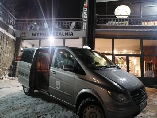 Srebrny van Mercedes z otwartymi drzwiami na tle budynku wypożyczalni sprzętu zimowego w nocy.