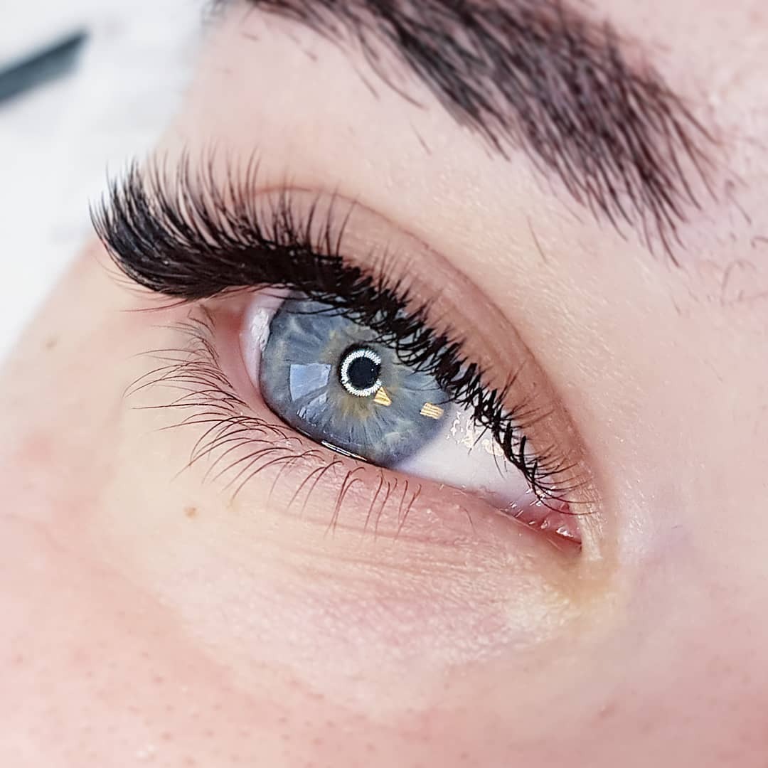 Zbliżenie na oko z przedłużonymi, gęstymi rzęsami, o niebieskiej tęczówce z widocznym odbiciem światła.