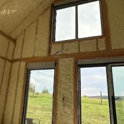 Wnętrze domu szkieletowego po ociepleniu pianką PUR, widoczne okna z widokiem na zewnątrz, drewniane elementy konstrukcyjne i fragment podłogi z deskami.