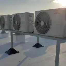 Trzy jednostki zewnętrzne klimatyzacji Hyundai zamontowane na metalowej konstrukcji na jasnym dachu, widoczne w promieniach zachodzącego słońca.