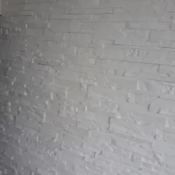 Ściana wykończona białymi, podłużnymi płytkami imitującymi kamień, ułożonymi w poziomych pasach, z delikatną fakturą i nierównomiernym oświetleniem.