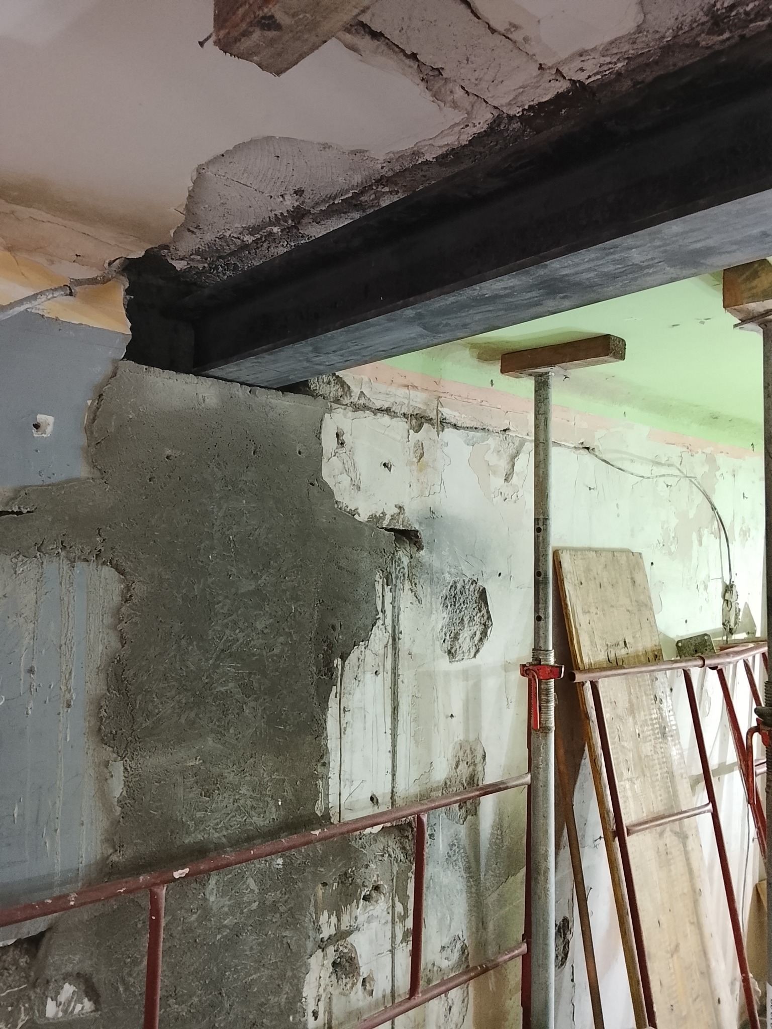 Wzmocnienie konstrukcji stropu z użyciem stalowej belki i podpór. Ściana częściowo otynkowana, widoczne ślady wcześniejszych prac. Prace remontowe w trakcie.