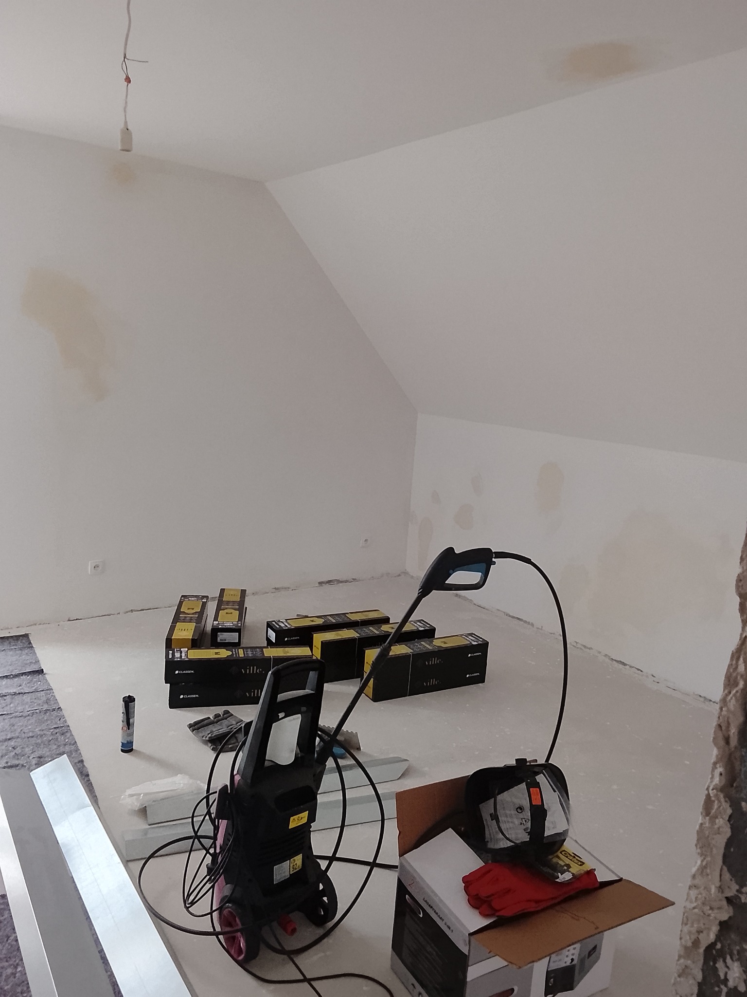 Poddasze w trakcie prac wykończeniowych: widoczne plamy na ścianach, narzędzia, kartony z panelami podłogowymi. Przygotowania do remontu.