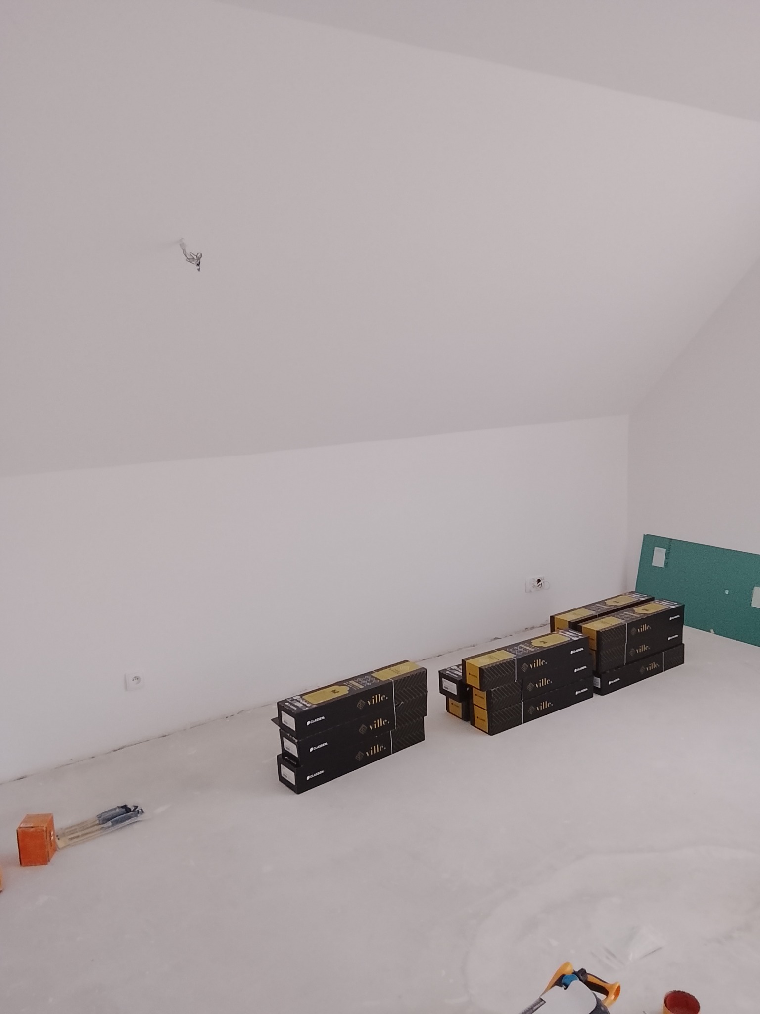 Poddasze w trakcie prac wykończeniowych: przygotowane paczki paneli podłogowych Classen Ville, narzędzia glazurnicze i płyta gipsowa. Białe ściany i wylewka podłogowa.