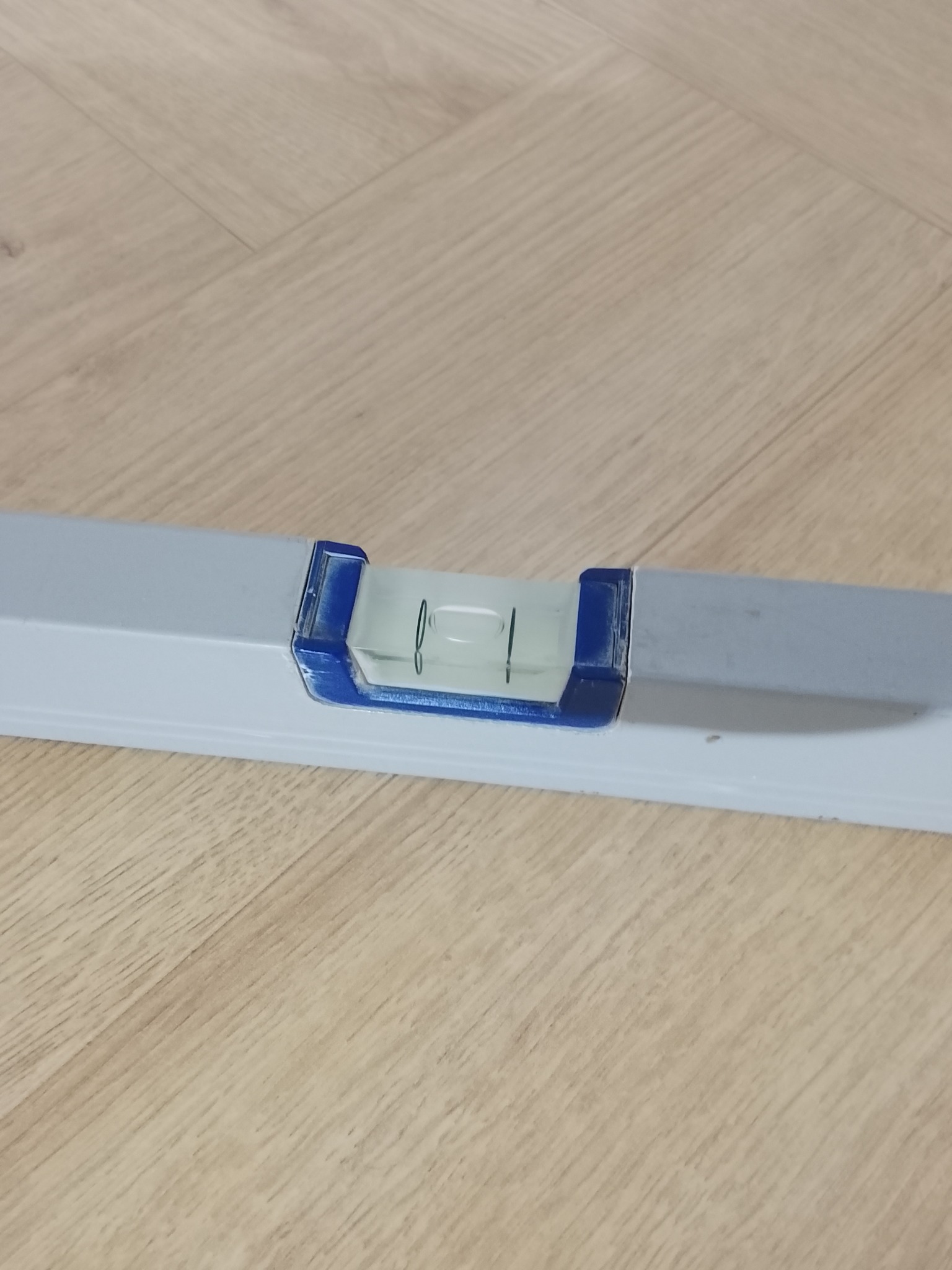 Poziomica w zbliżeniu na drewnianej podłodze, narzędzie do precyzyjnego ustawiania poziomu podczas prac wykończeniowych, z widocznym pęcherzykiem powietrza.