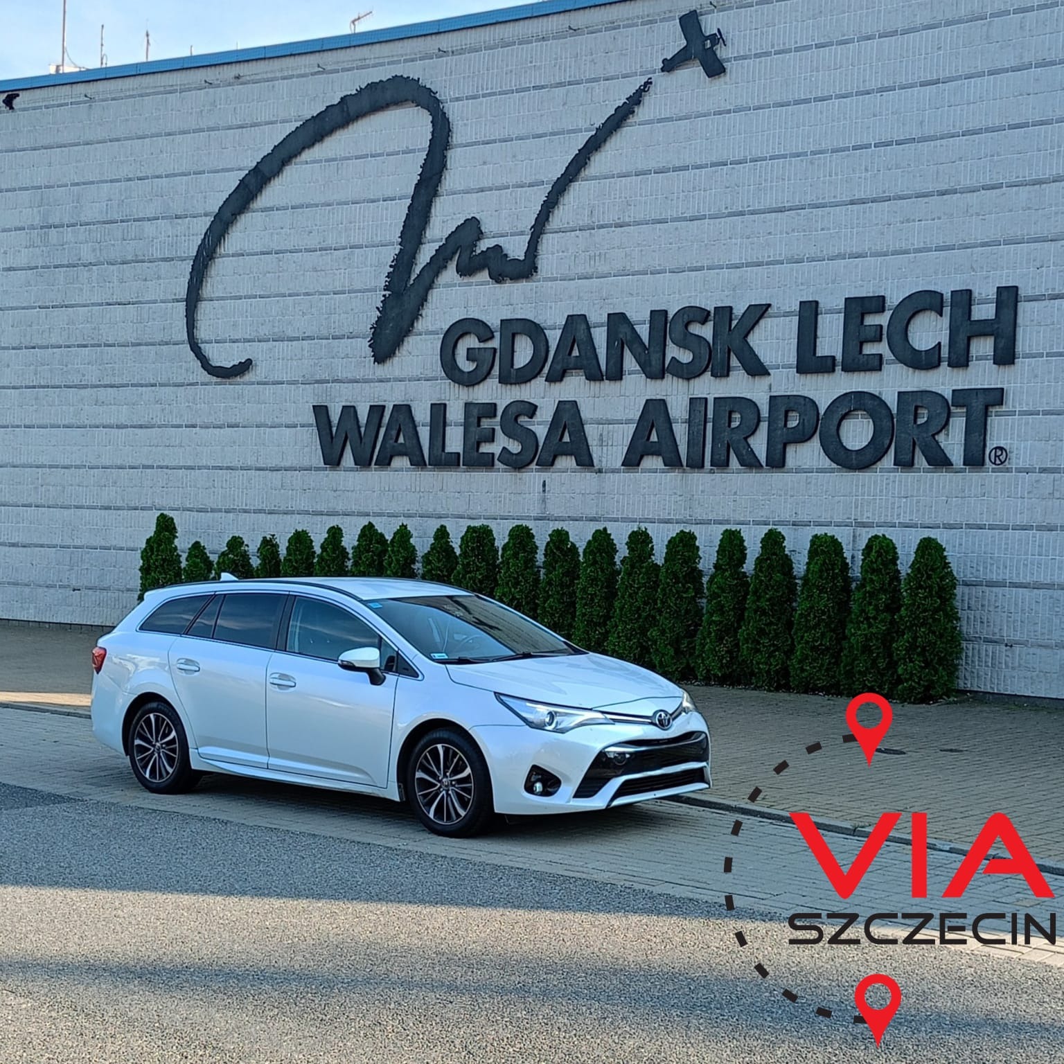 Białe kombi zaparkowane przed budynkiem lotniska Gdańsk Lech Wałęsa z napisem 'VIA Szczecin' na chodniku.