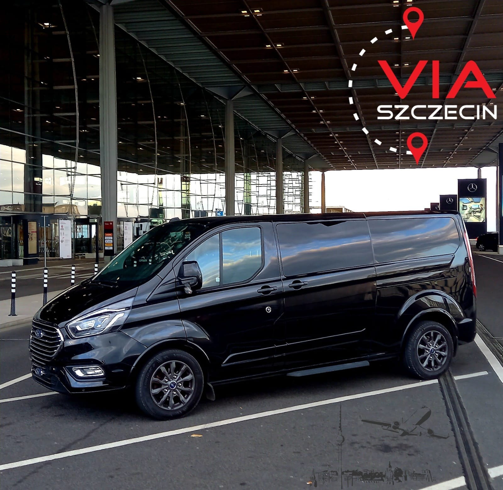 Czarny van Ford Transit Custom z przyciemnianymi szybami zaparkowany przed nowoczesnym budynkiem lotniska, z grafiką VIA Szczecin w rogu.