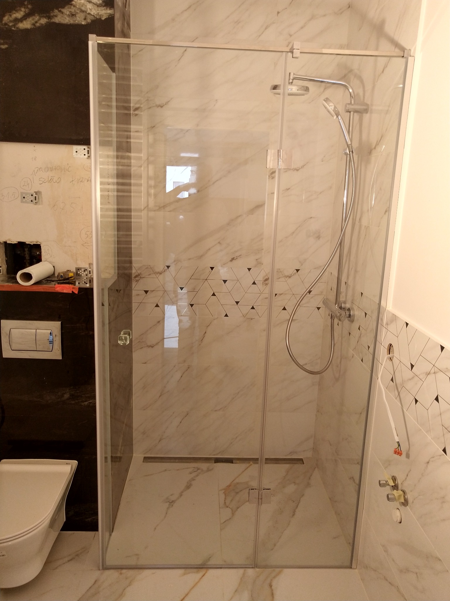 Nowoczesna kabina prysznicowa ze szkła hartowanego, widoczna podczas montażu, z niedokończonymi elementami instalacji wodnej i fragmentem toalety w tle.