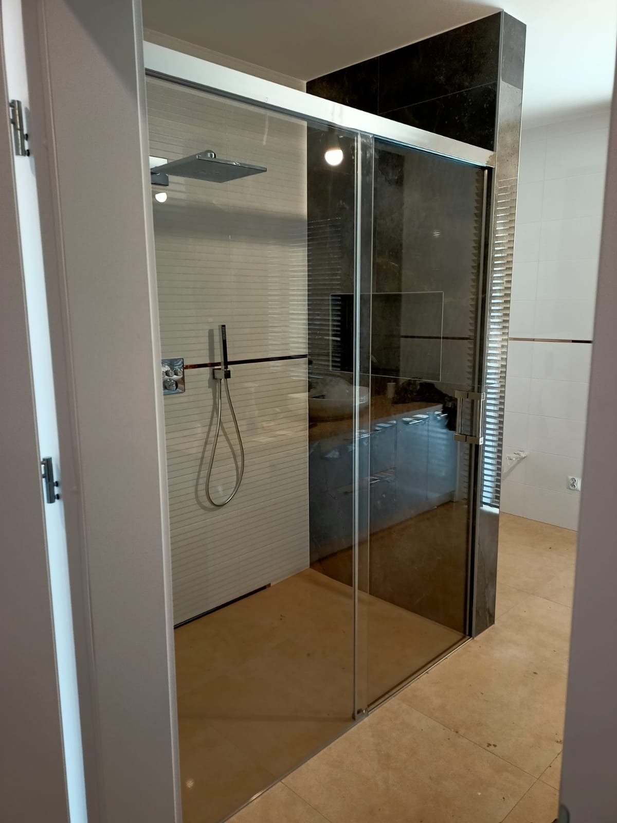 Nowoczesna kabina prysznicowa z przesuwnymi drzwiami ze szkła hartowanego, widoczny deszczownica, bateria natryskowa i płytki ceramiczne.