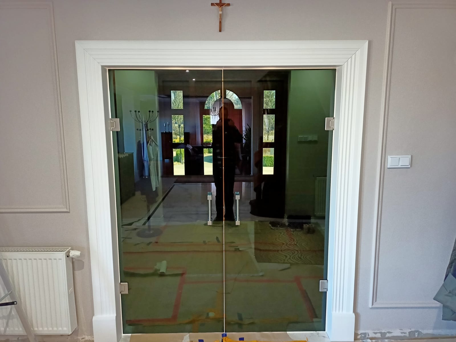 Szklane dwuskrzydłowe drzwi wewnętrzne z białymi futrynami, widoczne ślady po montażu na podłodze, w tle osoba w ciemnym ubraniu i fragment wnętrza domu.