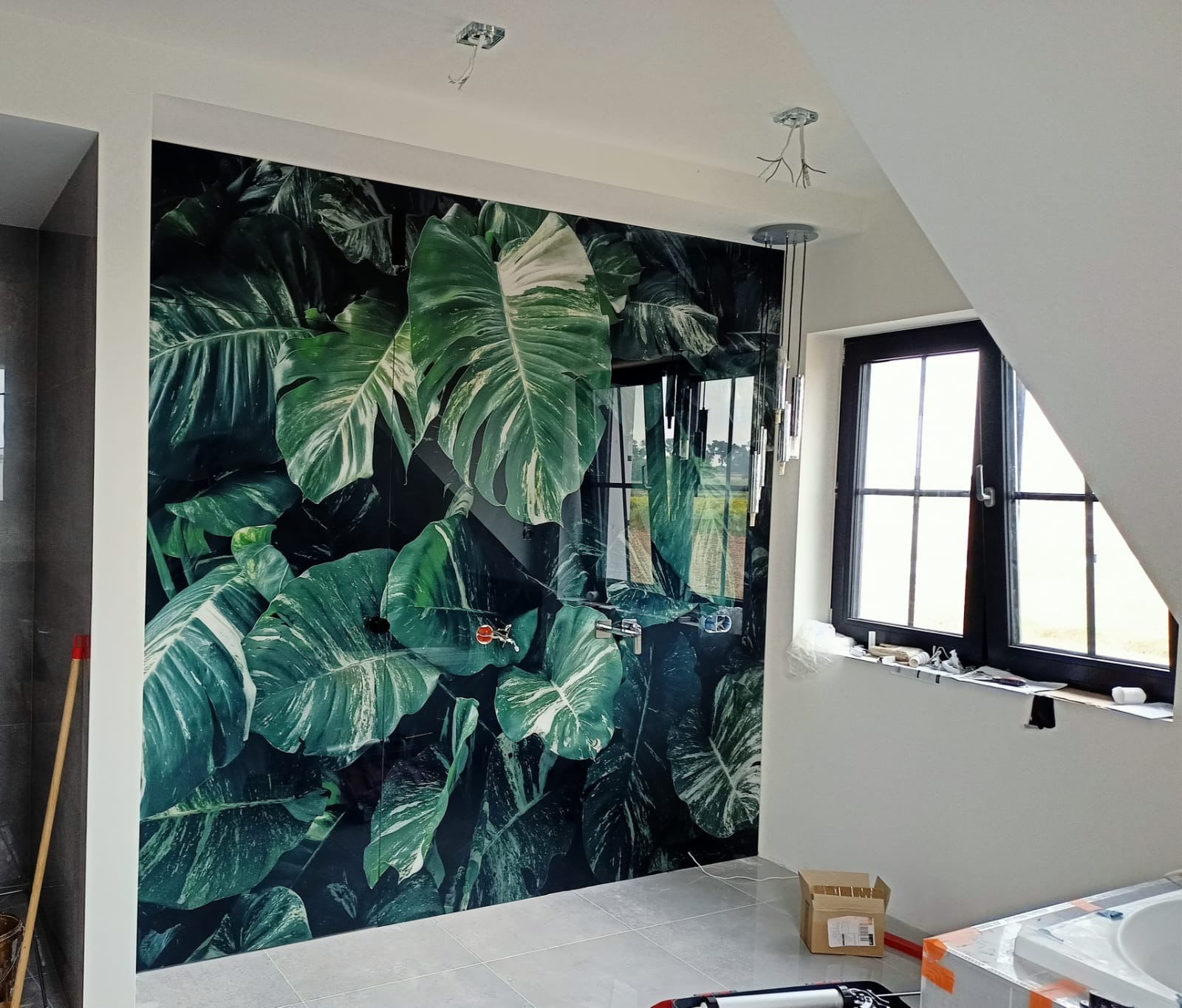 Szklana ściana prysznicowa z motywem tropikalnych liści w łazience w Kraśniku, widoczne baterie i fragment okna.