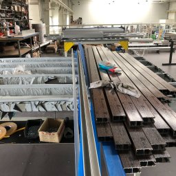 DOOR Filipek sp.k Producent ślusarki i stolarki budowlanej z aluminium i PCV - Produkcja profili aluminiowych o strukturze drewna w hali: detale cięcia, przygotowane elementy, narzędzia i akcesoria na stanowisku pracy.